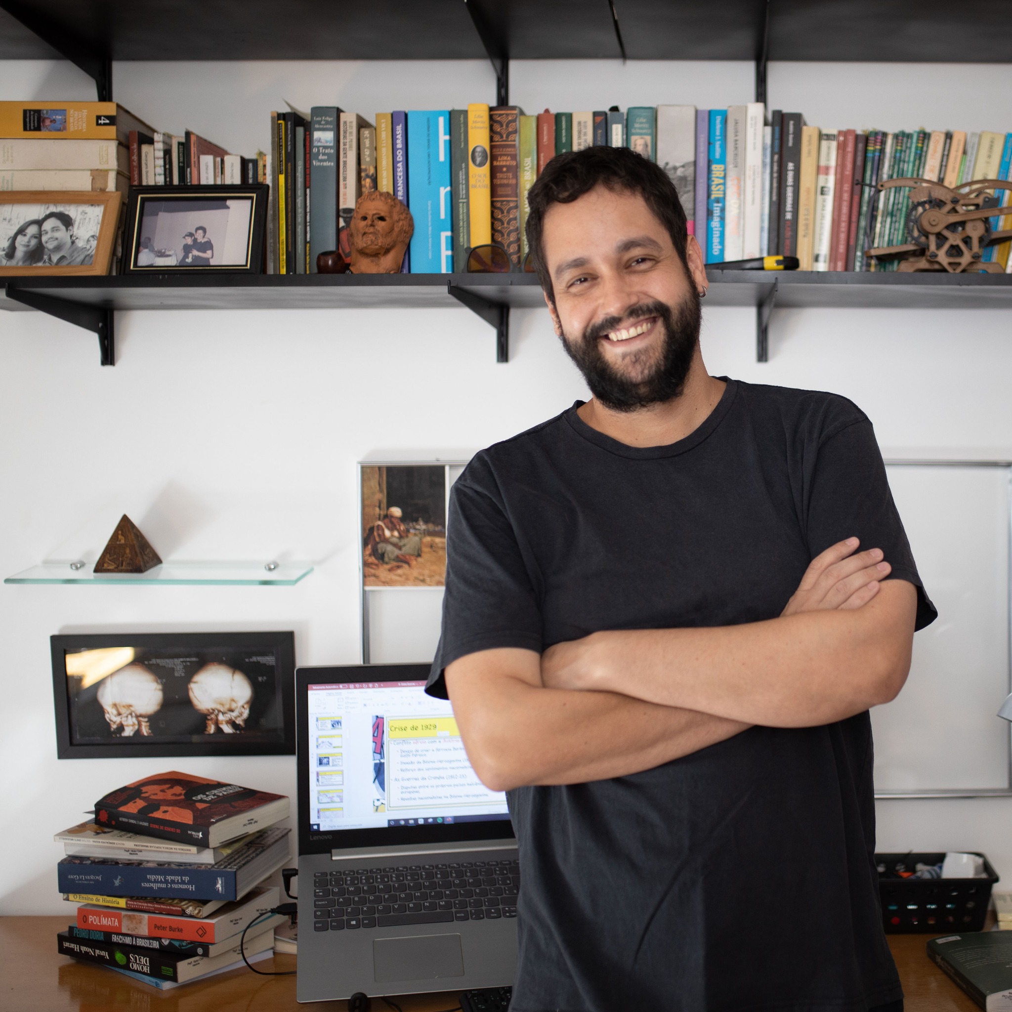 Victor Creti em seu espaço de trabalho, diante de uma estante de livros